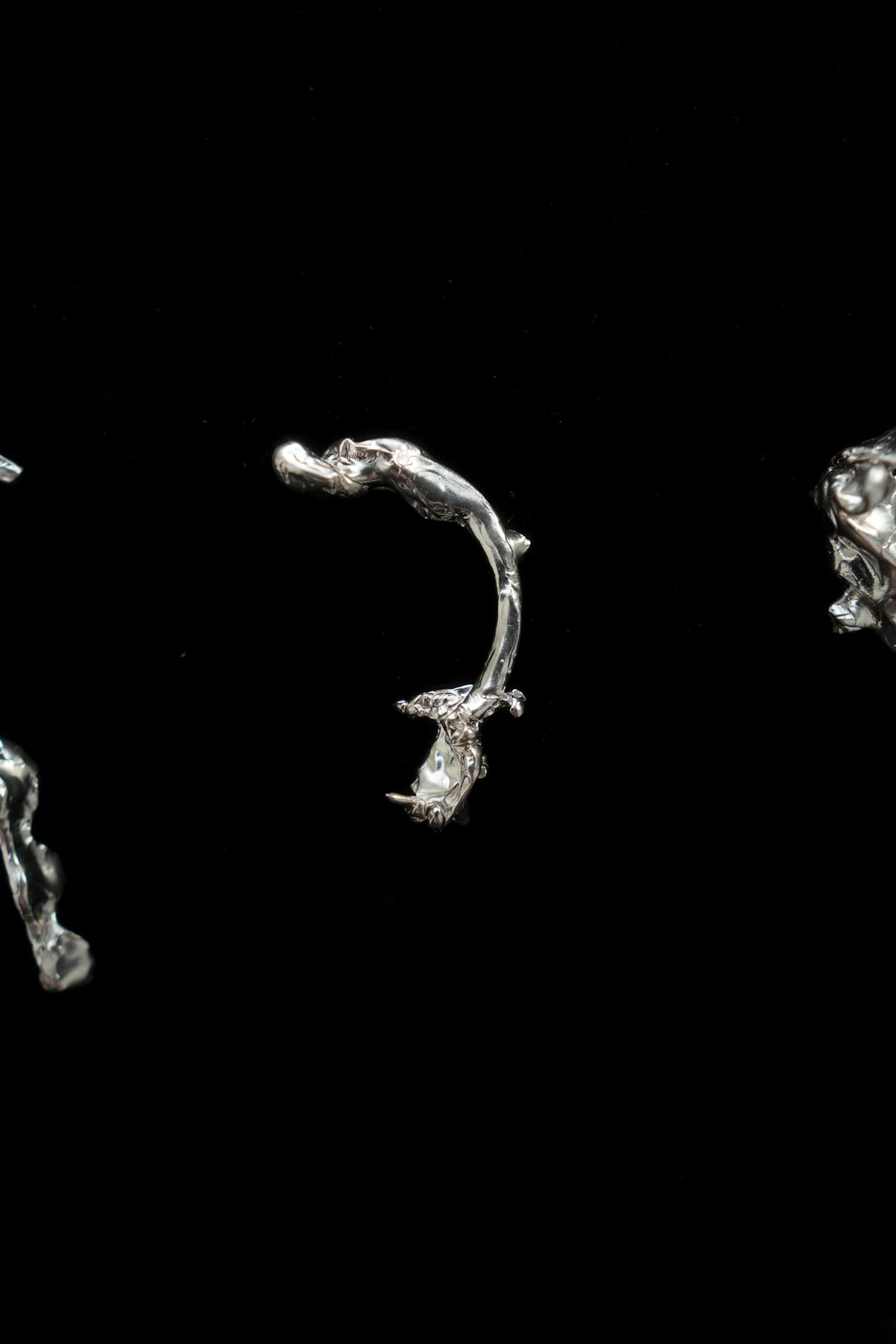 A close-up studio shot of a small silver-toned jewelry piece, likely a curved earring or pendant, on a solid black background.