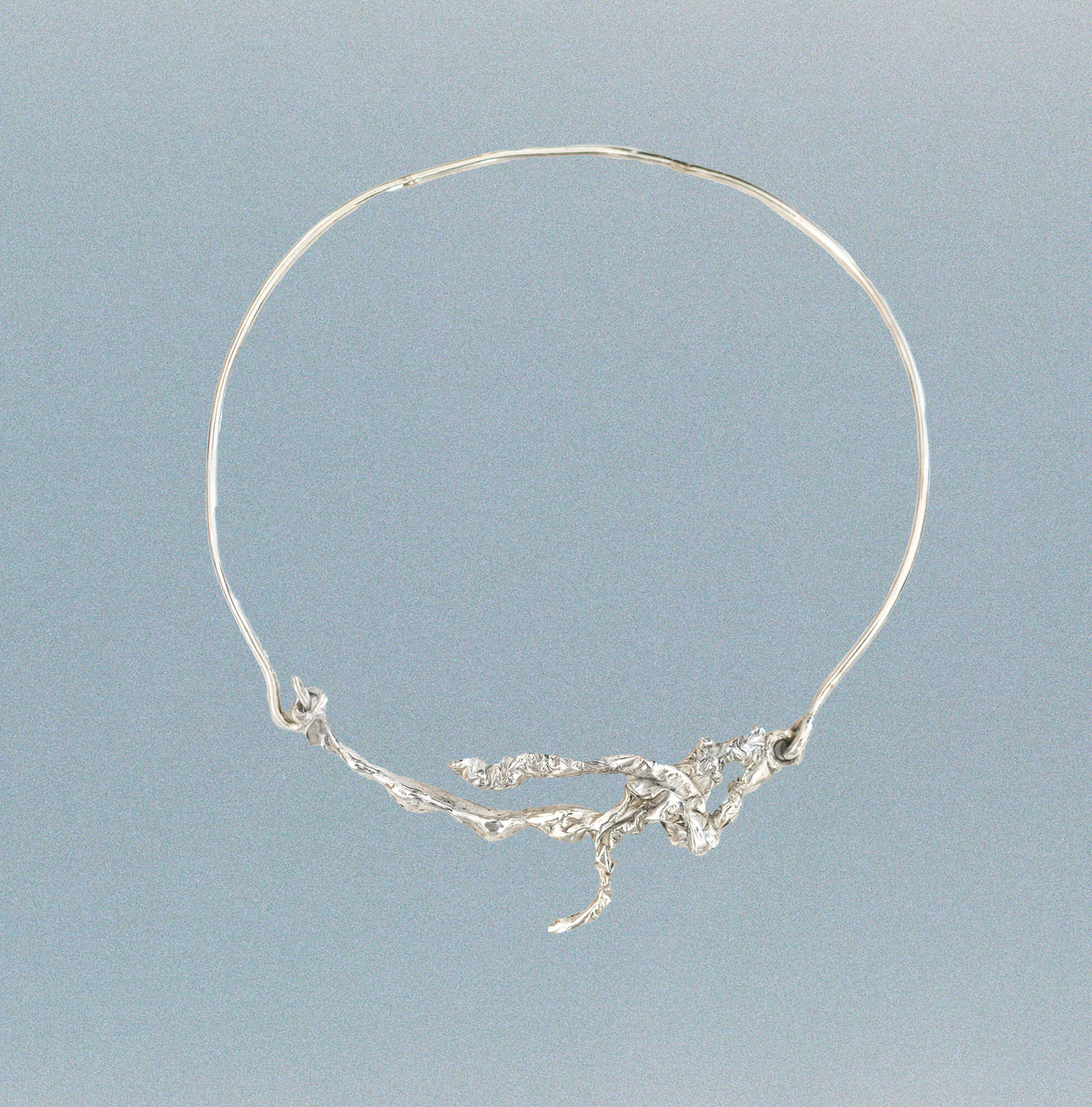 A delicate silver wire hoop necklace with an organic, branch-like cluster of solid sterling silver, displayed against a soft, light blue-gray gradient background.