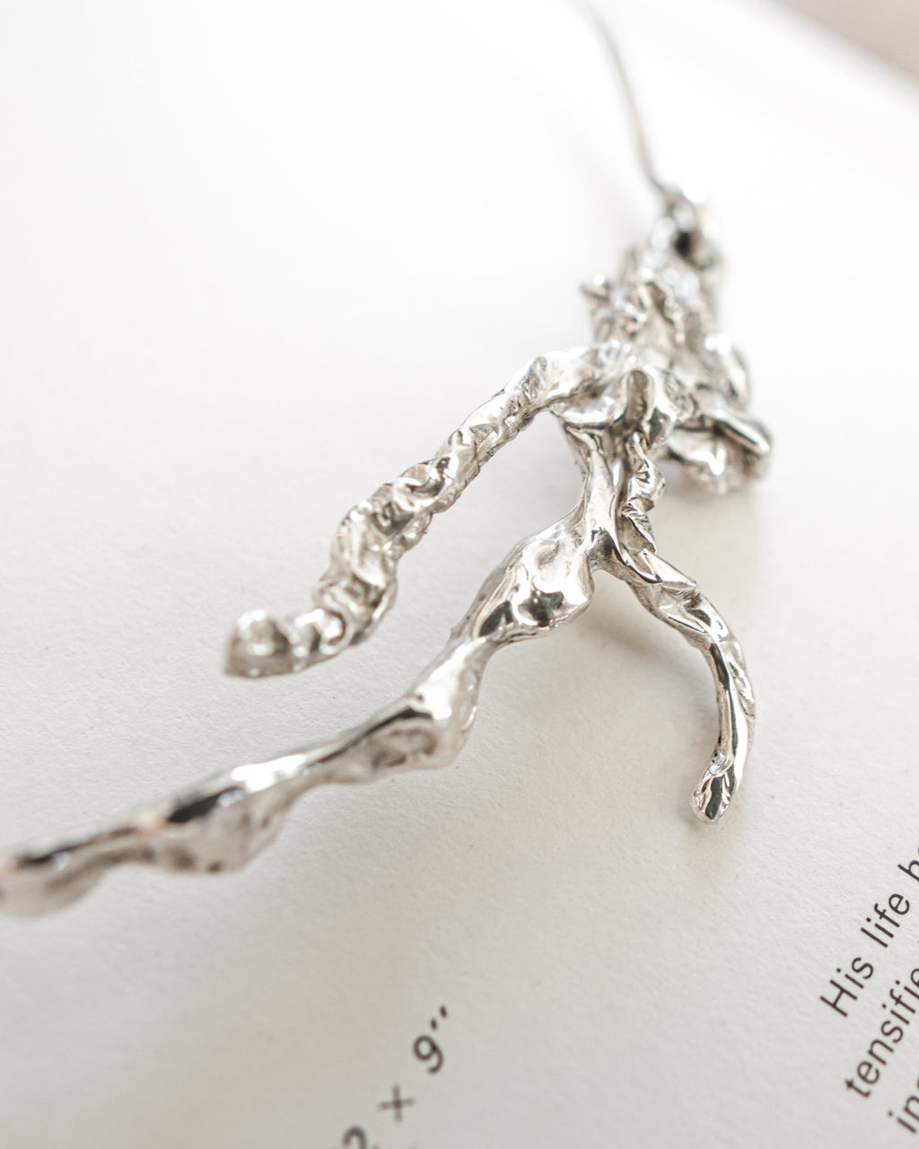 A close-up of a silver branch-shaped necklace resting on an open book page with printed text.