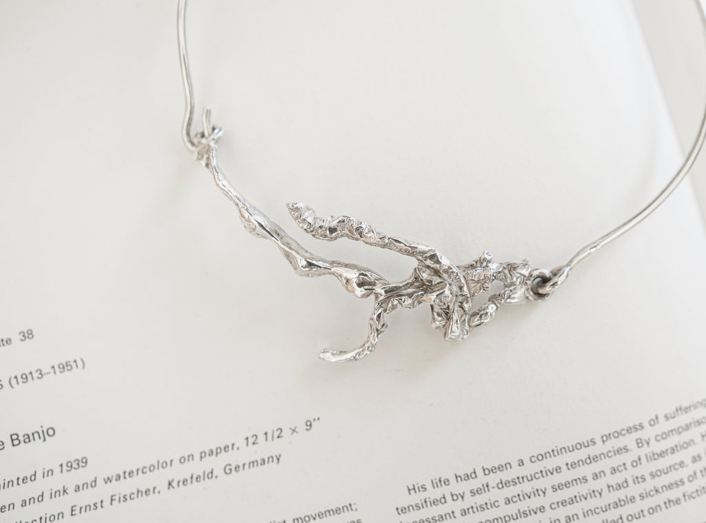 A silver abstract branch or tree-of-life style pendant necklace laid on an open book page with printed text visible.